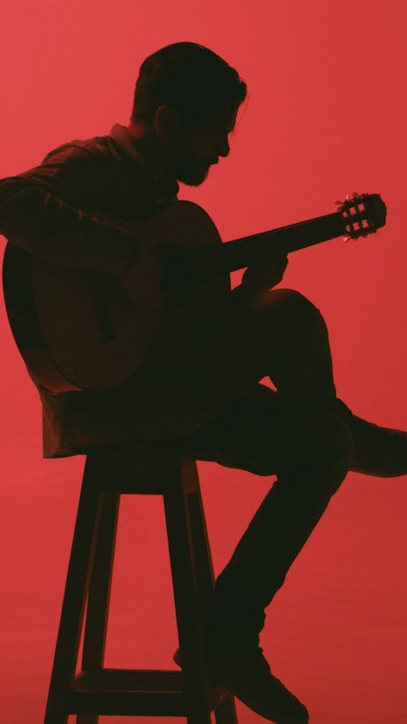 Silhouette of a guitarist playing sitting on a bench.