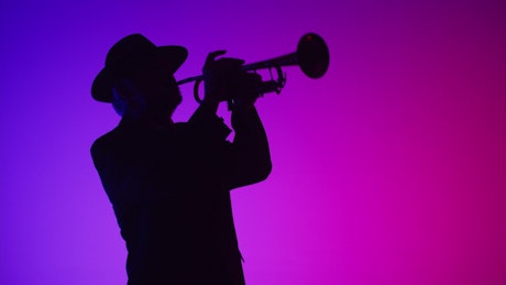Silhouette of a man playing a tune on a trumpet against neon lights.