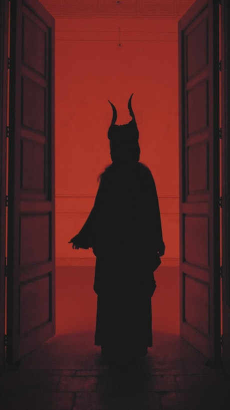 Silhouette of a person with horns and robe under a red light.