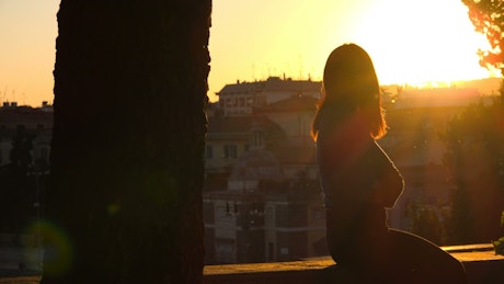 Silhouette of a woman at sunset looking out over a town.