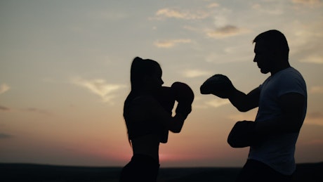 Silhouette of a woman working out with her trainer at sunrise.