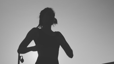 Silhouette of a young woman jogging in front of the sun.