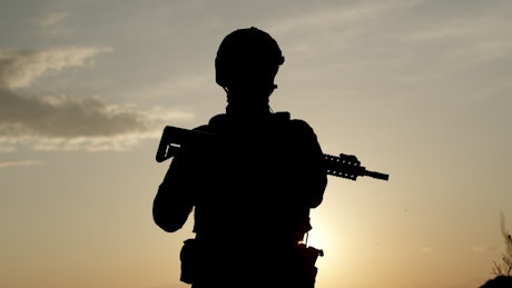 Silhouette of an armed soldier looking into the distance.