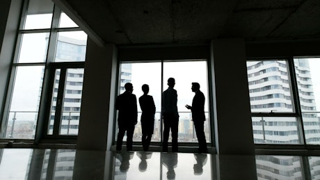 Silhouette of business people talking by highrise window.