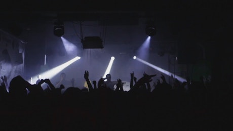 Silhouette of concert crowd waving arms and jumping.