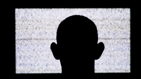 Silhouette of the shaved head of a man in front of a tv.