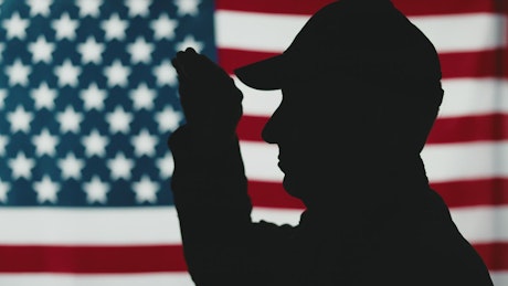 Silhouette of war veteran saluting with U.S. flag in background.