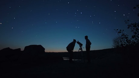 Silhouettes of a couple of men and a telescope.