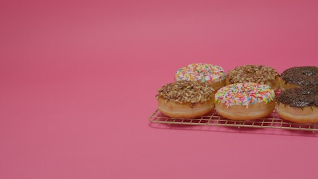 Six glazed donuts on a pink background.