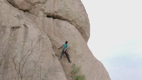 Skilled alpinist climbing a gigantic rock.