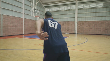 Skilled basketball player shooting baskets, training alone.