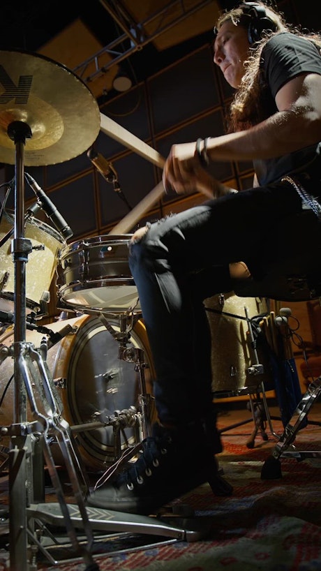 Skilled drummer wearing headphones moves his feet fast while jaming on a music studio.