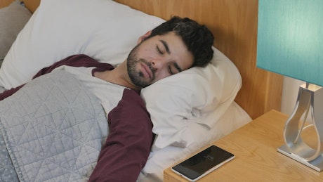 Sleeping man is awakened by his cell phone alarm.