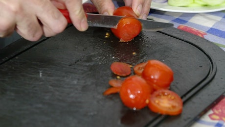Slicing tomatoes on a black chopping board.