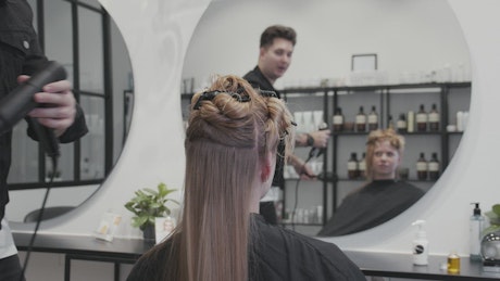 Slow motion hairdresser blow drying young woman's long blonde hair.