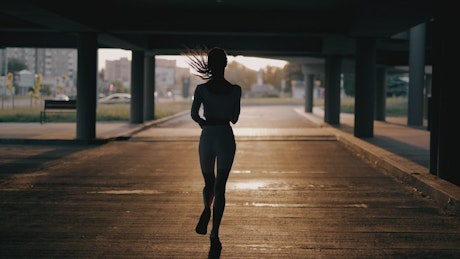 Slow motion of a woman running under a city bridge.