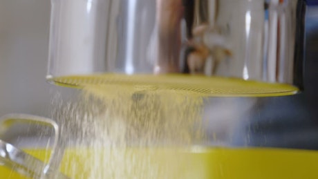 Slow motion sifting flour through a metal sieve.