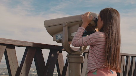 Small girl having fun with binoculars looking at the city.