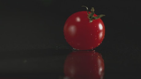 Small, juicy cherry tomato bouncing against a dark surface.