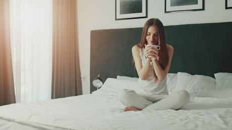 Smiling woman enjoying morning coffee in bed.