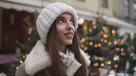 Smiling woman enjoys winter snowflakes in street