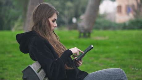 Smiling young woman on bench uses digital tablet.