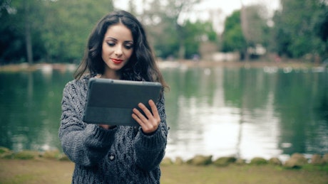 Smiling young woman using a tablet in front of a pond.