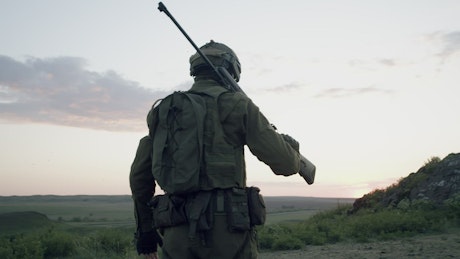 Soldier with a rifle on his shoulder walking across a field.
