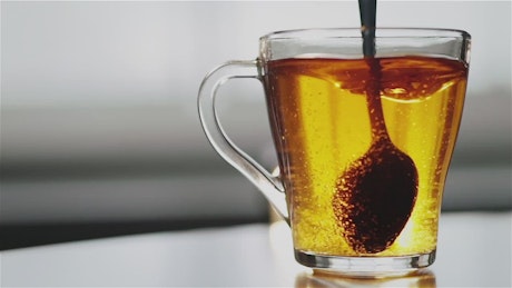 Spoon stirring sugar in clear glass tea cup.