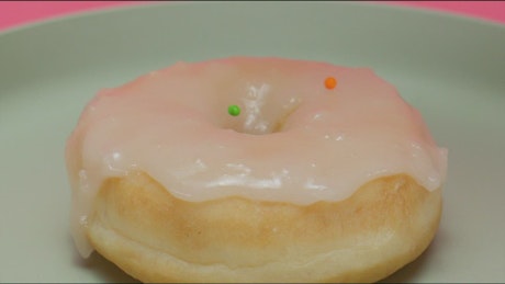Spreading colorful pieces on a glazed donut.