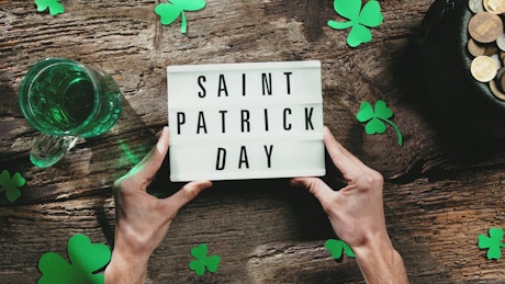 St. Patrick's Day sign being placed on a festive wooden background.