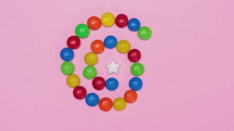 Star candy surrounded by chocolates on a pink background