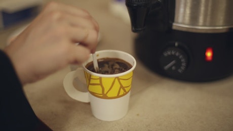Stirring milk and sugar into a paper coffee cup.