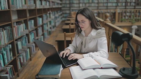 Student doing research in university library with books and laptop