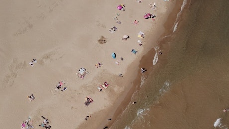 Sunbathers along a beach from drone view.