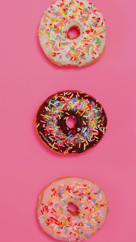 Taking three glazed donuts in a row on a pink background.