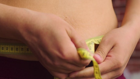 Tape measure being pulled tight across a stomach.