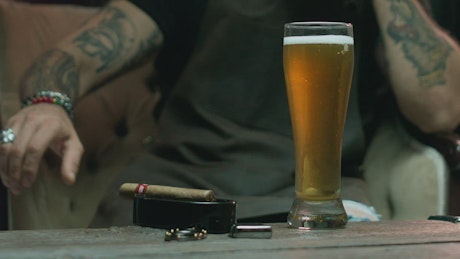 Tattooed man drinking beer with a cigar.