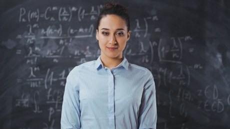 Teacher smiling in front of a blackboard.