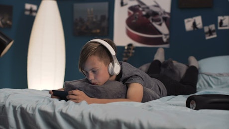 Teen boy playing on his phone on the bed.
