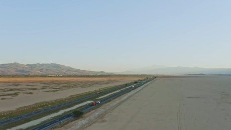The vehicles cross the asphalt highway beside the breathtaking desert landscape with a backdrop of mesmerizing mountains.