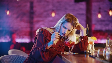 Thoughtful woman playing with her drink in a bar