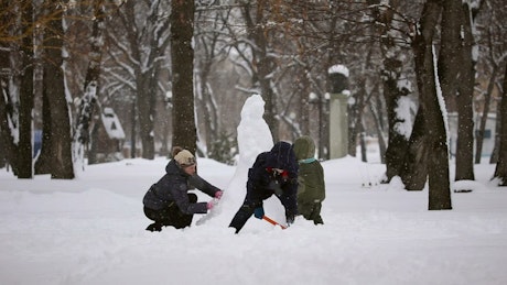Three children build a snowman in the snow.