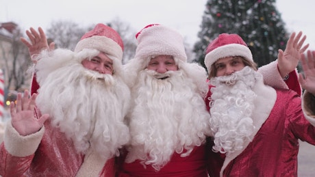 Three funny Santa Clauses waving at the camera on christmas day.