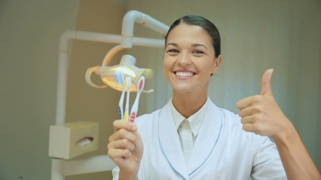 Thumb up of a dentist showing toothbrushes