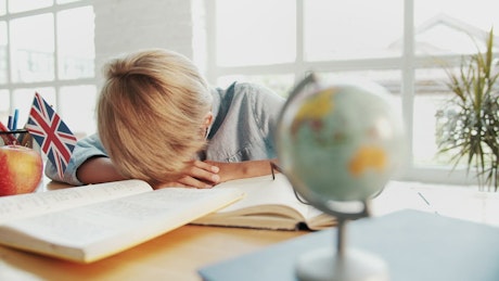 Tired boy wakes up after falling alseep on desk in classroom