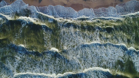 Top aerial view of the sea waves reaching a beach.