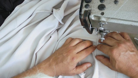 Top view of a tailor's hand sewing a shirt.