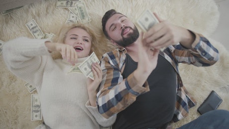 Top view of rich couple on rug laying in money.
