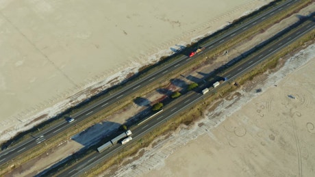 Trucks and cars crossing a straight highway with a dry lake on the sides.